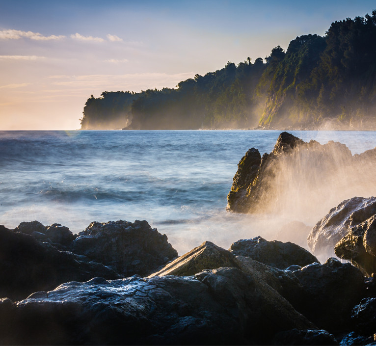 Hilo waves crashing into lava rock with mountains in the background