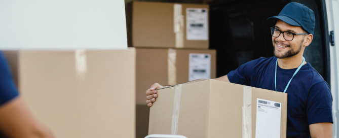 Young happy delivery man unloading boxes from a mini van and talking with his coworker.