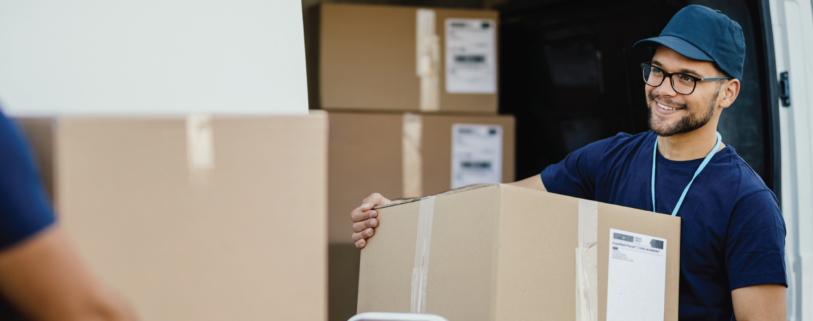 Young happy delivery man unloading boxes from a mini van and talking with his coworker.